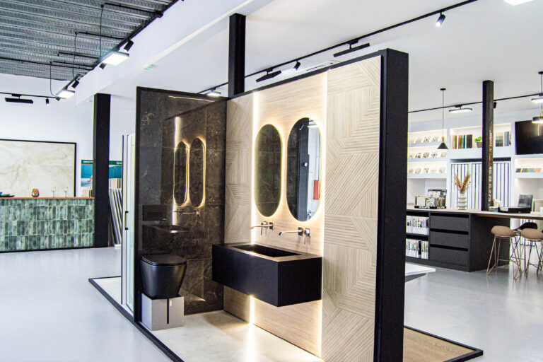 Baño moderno con lavabos suspendidos, espejos retroiluminados y revestimientos cerámicos en tonos madera y mármol. Diseño elegante en el showroom de Ari Ceramic Córdoba.